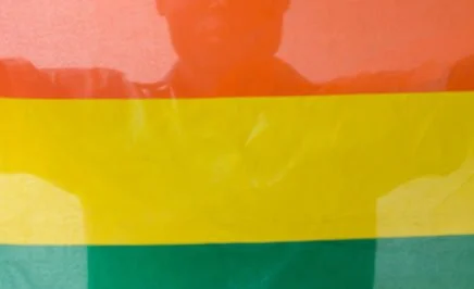 Shadow of a man standing behind a rainbow pride flag.