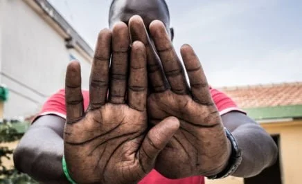 A young man from Gambia holds his hands in front of the camera, covering his face