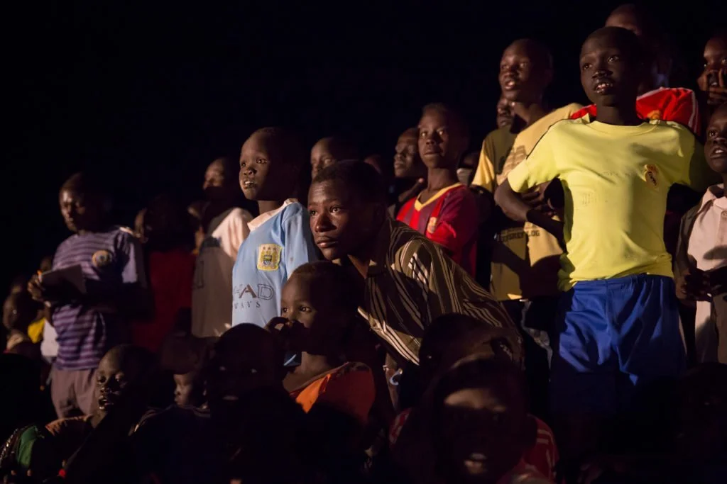  a group of young people standing together at night time look eagerly past the camera