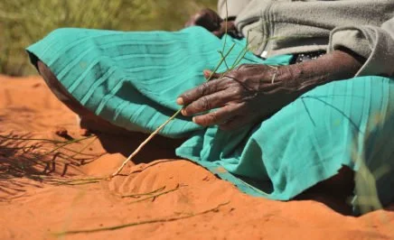 Aboriginal woman making a sand painting in NT, Australia.