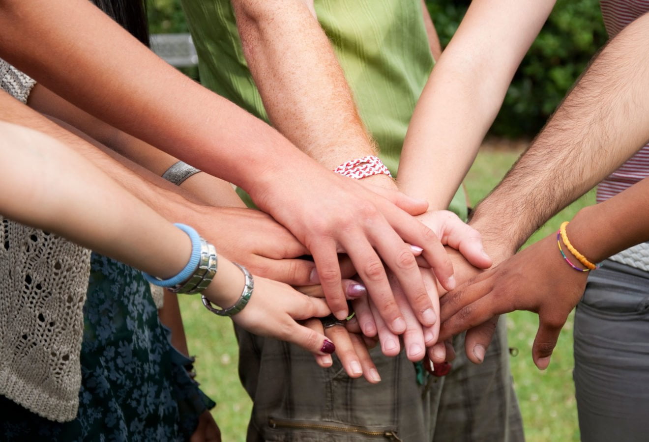 The arms of several people are stacked in the center of the image. © iStock/cate_89