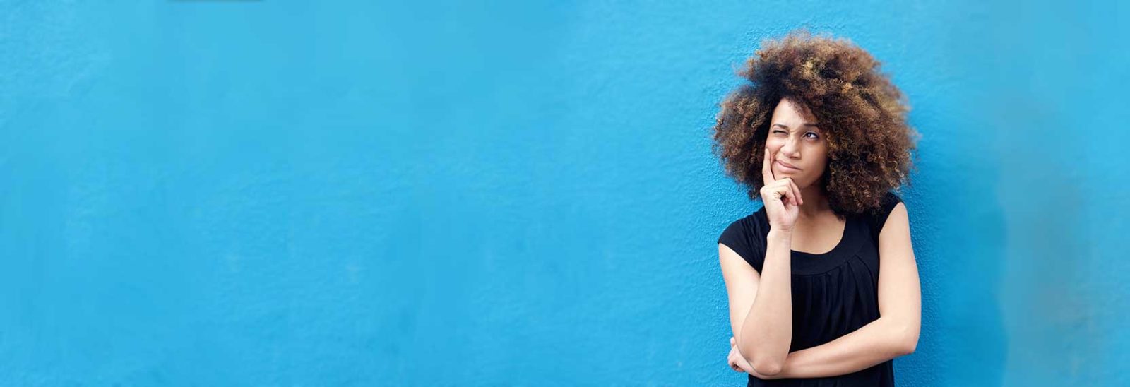 A woman standing in front of a blue wall deep in thought. © iStock/m-imagephotography