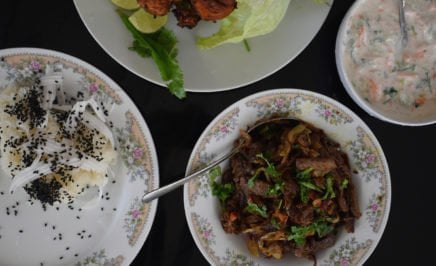 A bowl of crispy beef next to rice and yoghurt dressing