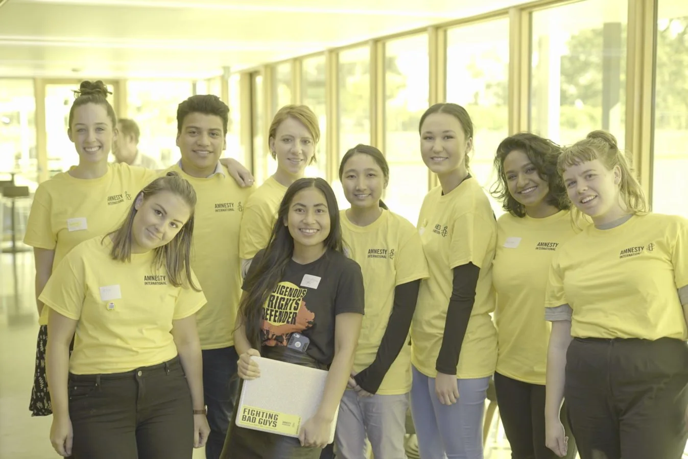 A group of volunteers wearing Amnesty yellow volunteer Tshirts & on in a black Indigenous Rights Tshirt are posed for the photo