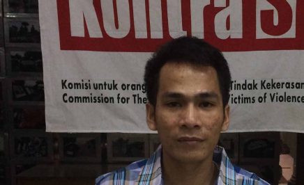 Yusman Telaumbanua, an Indonesian man released from death row, staring into the camera and holding an Amnesty International sign.