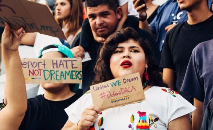 A close up photograph of protesters at a rally against ending the Deferred Action for Childhood Arrivals (DACA) programme in Los Angeles in 2017. The image shows a young women standing at the front of the crowd holding a sign that says 'United We Dream, #DefendDACA, equality'. Another sign, held up by a young man says 'Deport hate, not Dreamers'. In the background of the image is a young girl on her father's shoulders staring straight at the camera.