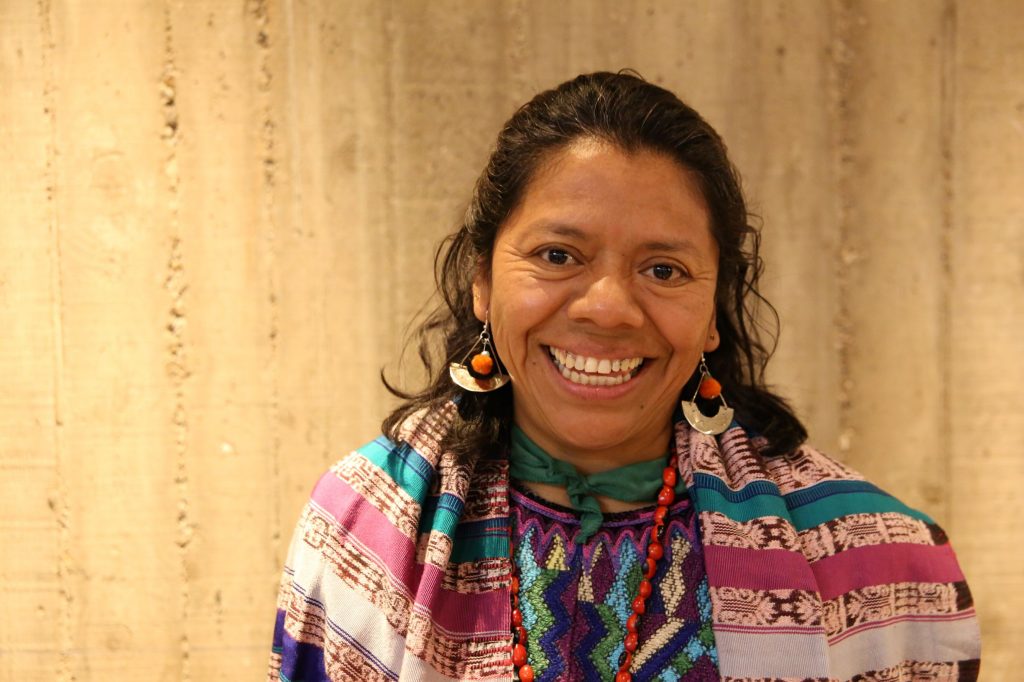 A woman wearing colourful, traditional clothing and jewellery from Guatemala, smiling widely