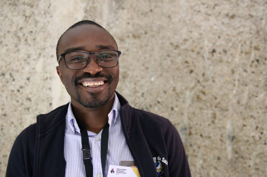 A dark-skinned young man with glasses and a big smile
