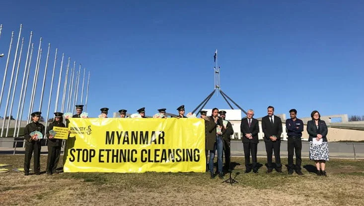 A group of people stand on the lawns at Parliament House in Canberra with a banner that says 'Myanmar stop ethnic cleansing'.