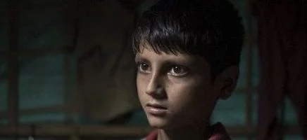 A young Rohingya boy holds a school book in a refugee camp in Bangladesh.