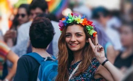 A woman wears a rainbow flower crown and performs the peace sign.