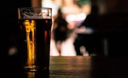 A pint of beer sitting on a wooden bench in a dark-lit room