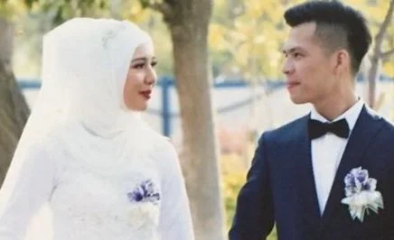 Mehray and Mirzat on their wedding day. Mehray wears a white wedding dress and hijab, Mirzat wears a black blazer. They are looking at each other.