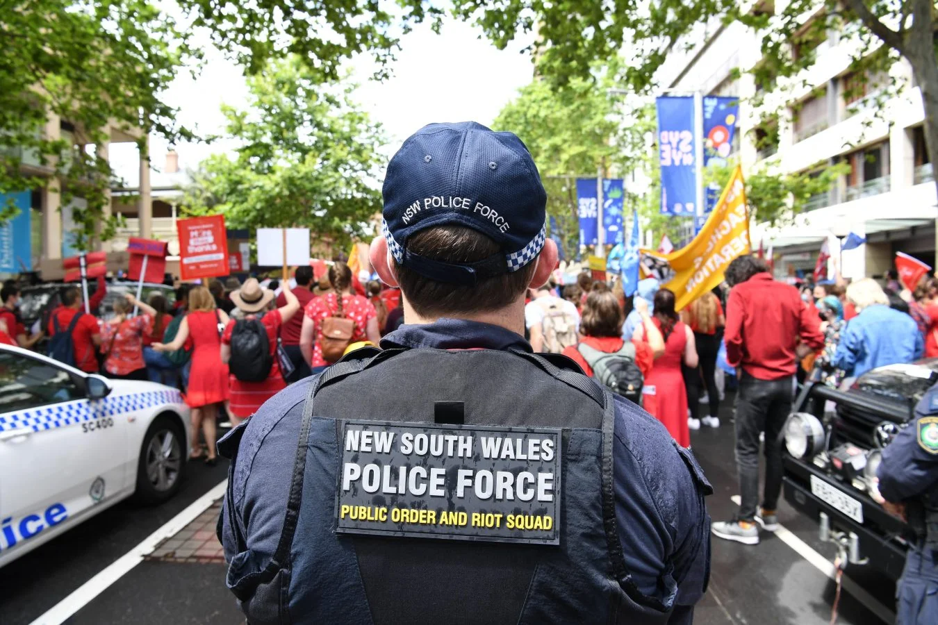 NSW Police Riot Officer stands behind a crowd of protester dressed in red and with banners