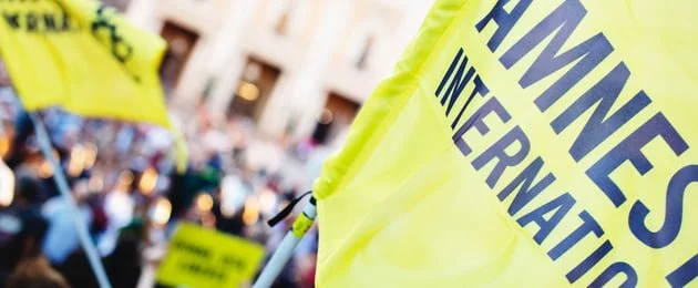 A close up of the Amnesty International flag someone is waving as part of a protest.