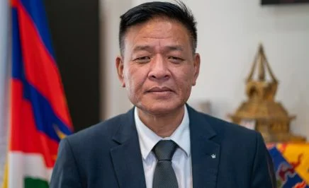 A photo of Penpa Tsering, a Tibetan man with dark hair, in a suit sitting at a desk.