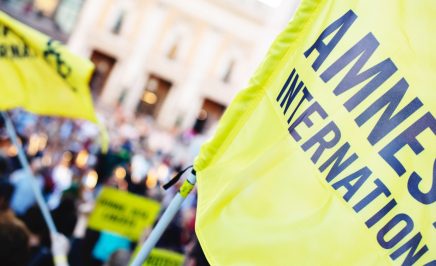 A close up of the Amnesty International flag someone is waving as part of a protest.